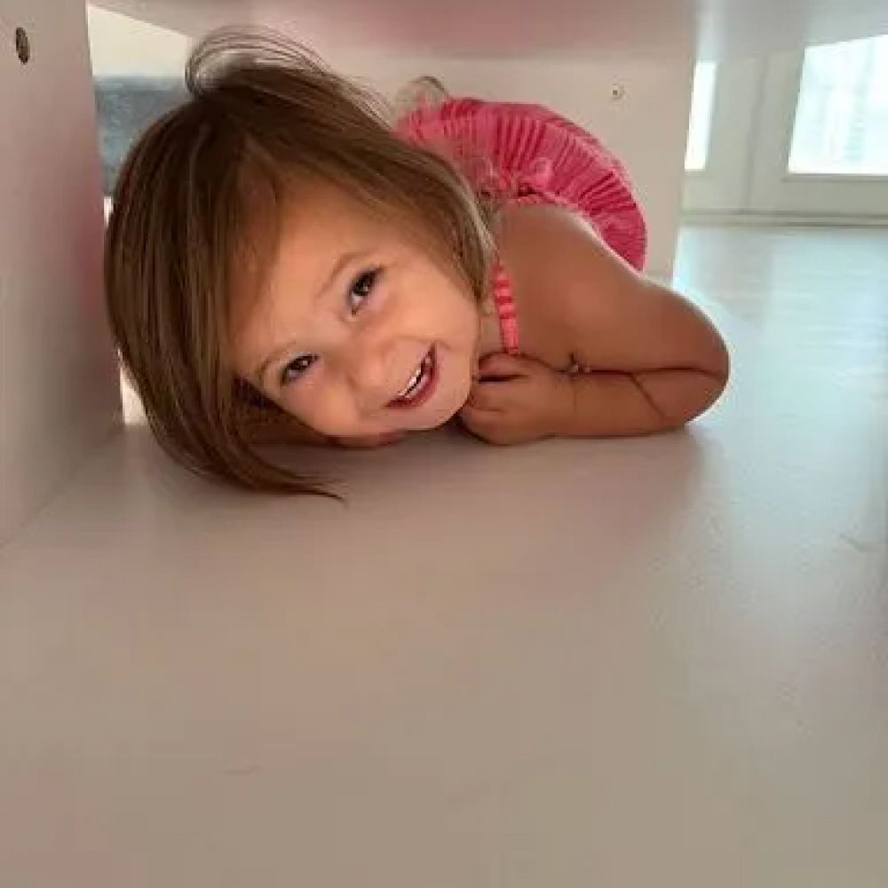 Child smiling under furniture with playful expression.