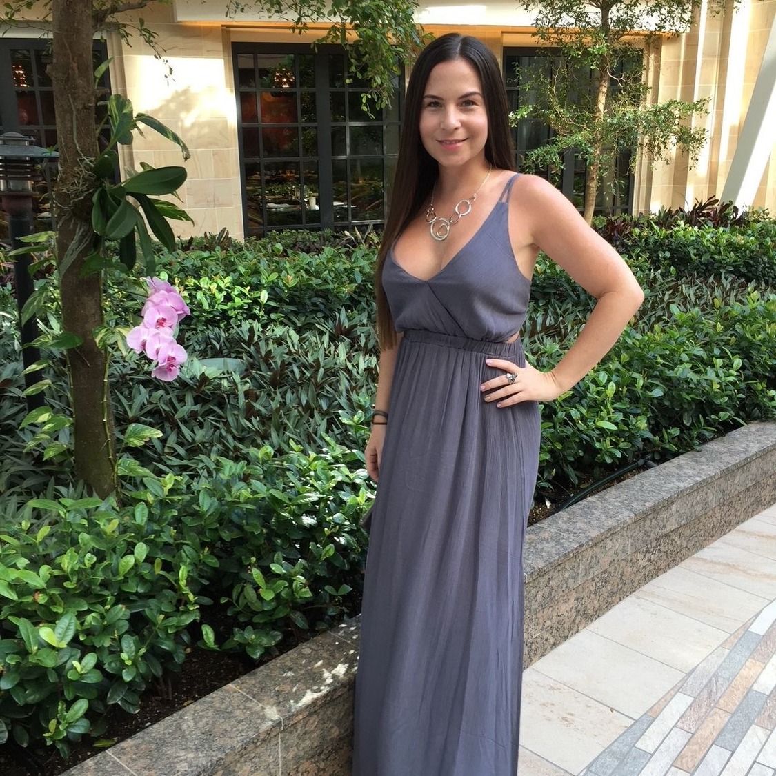 Woman in gray dress standing among greenery.