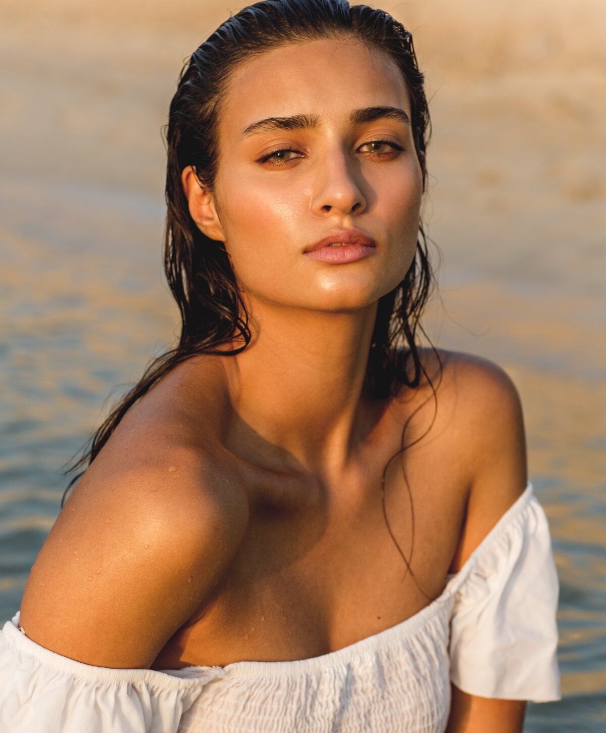 Woman with wet hair by the water at sunset.
