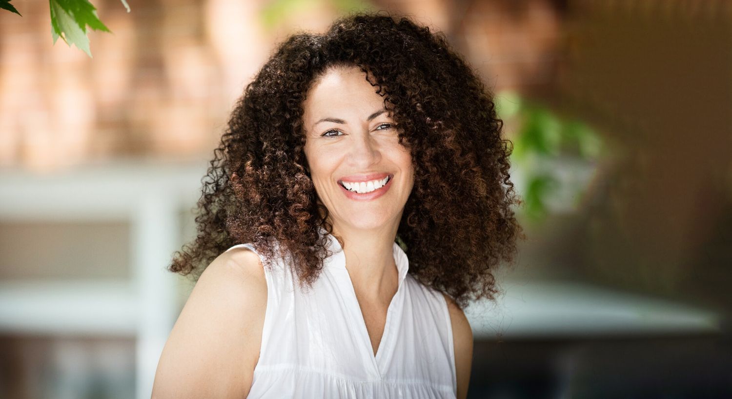Smiling woman with curly hair in bright setting.